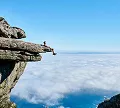 A man sits on a rock, gazing out at the vast ocean under a clear blue sky